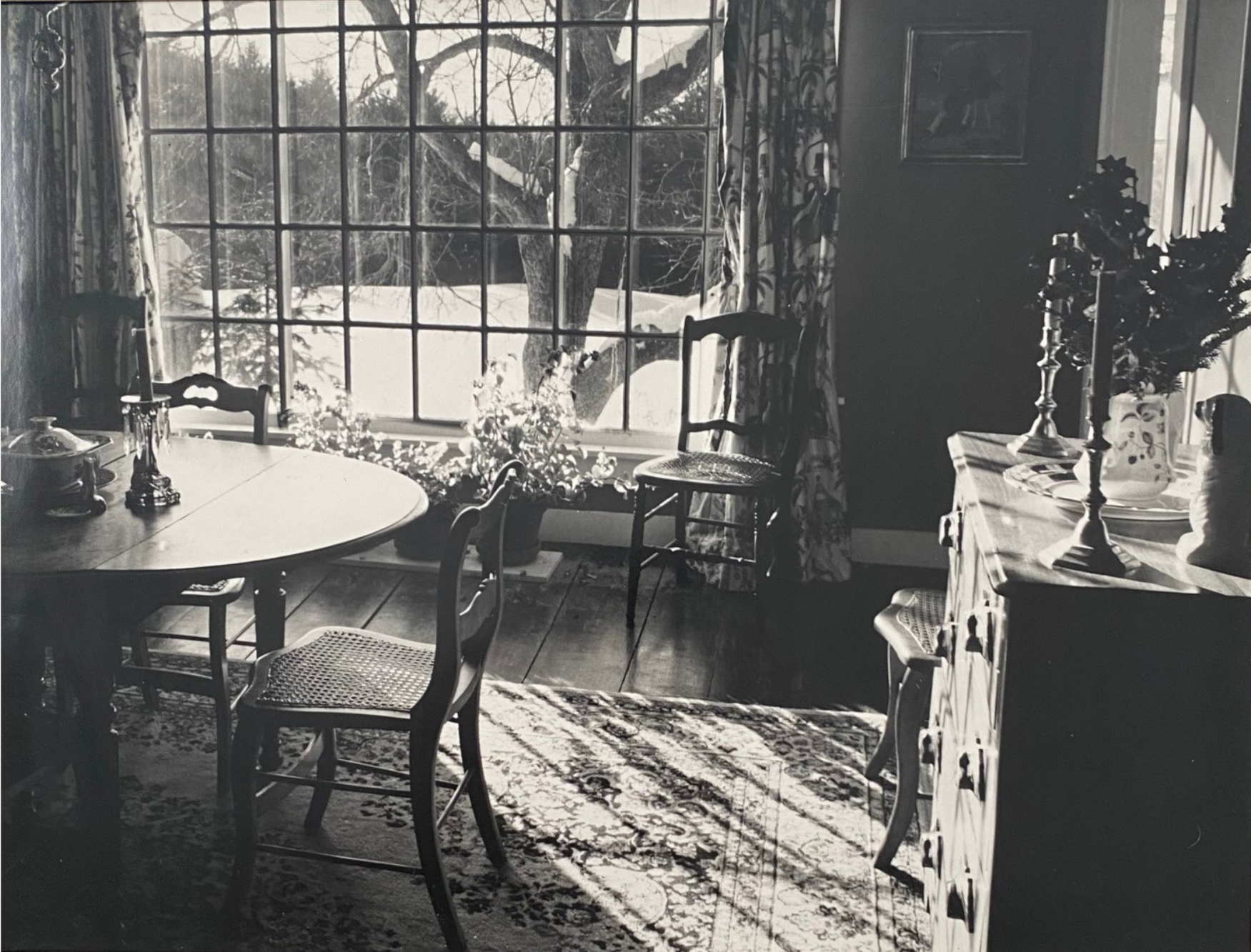 black and white image of a dining room filled with antiques lit by a large picture window. Reproduction of Janet Lee Chauncey's photograph,
