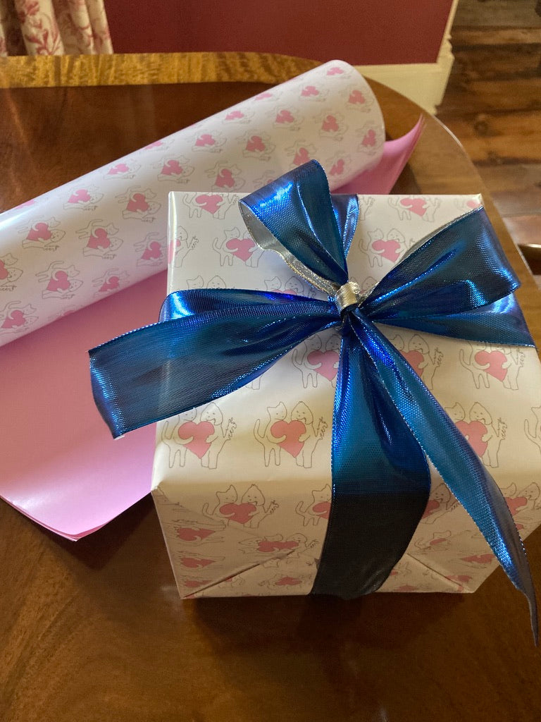 A large square present is wrapped in Sharing A Big Heart wrapping paper. The gift is placed near a vase with hydrangea flowers.
