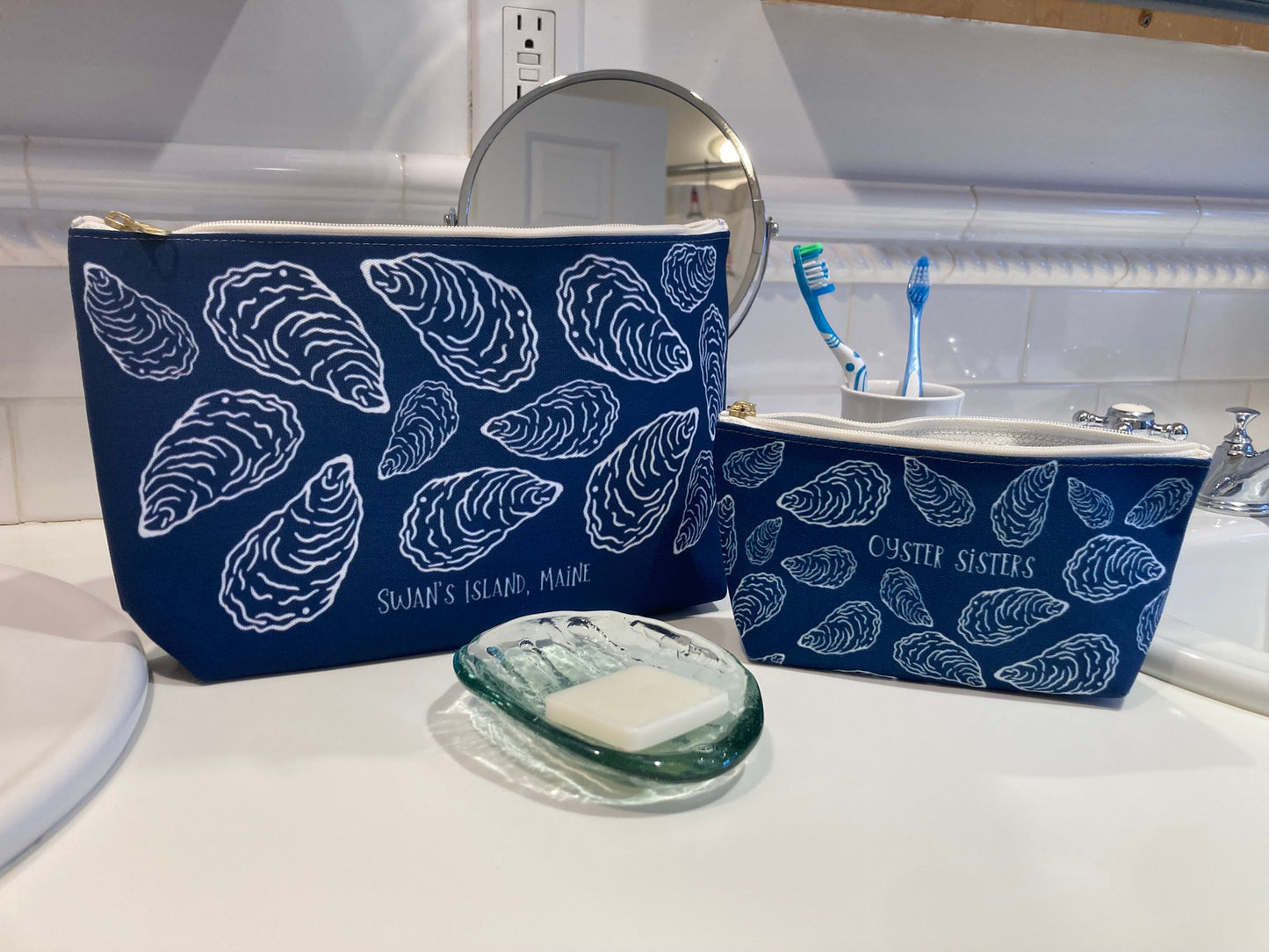 Two blue pouches with white shell pattern on a bathroom counter.
