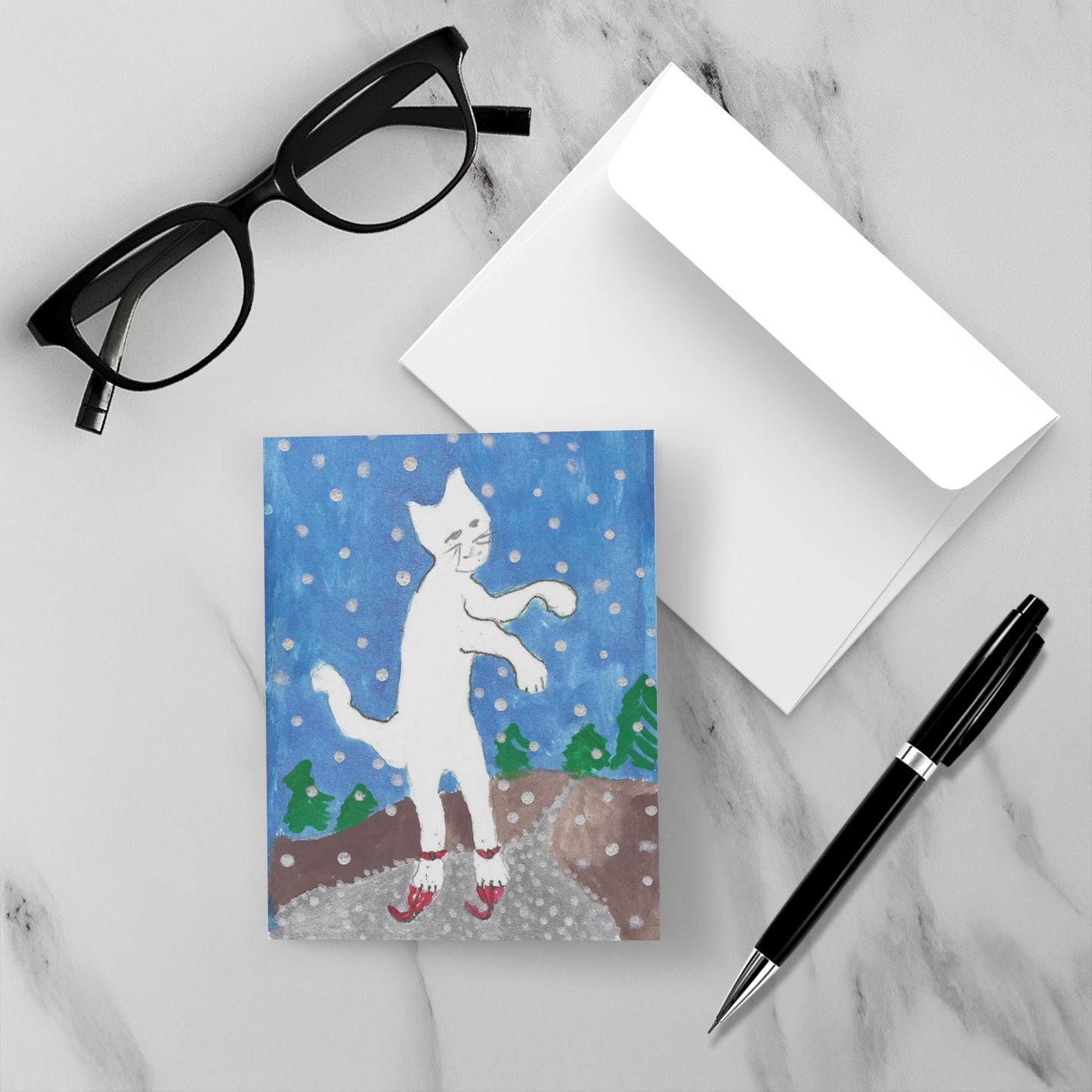 Mockup of the greeting card titled Caspar On Skates which displays the greeting card on a grey marble surface with a white envelope, Black glasses and a black pen.