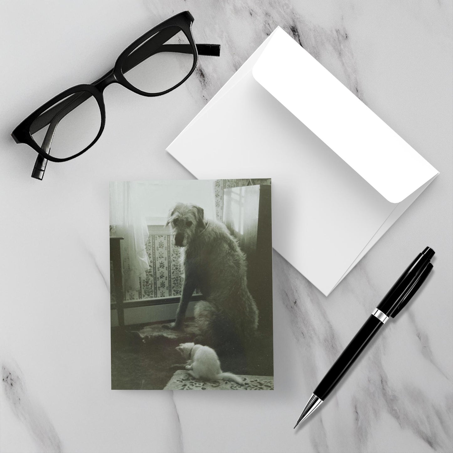 Positioned on a white marble backdrop are the front of the card Grizzy and Roxanne along with the envelope, a pen and reading glasses.