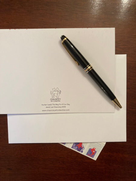 The back of the greeting card Hunter Leads The Way For A Fun Day is displayed on a brown desk with a white envelope, a black pen and a sheet of winter postage stamps peeking out from under the envelope.