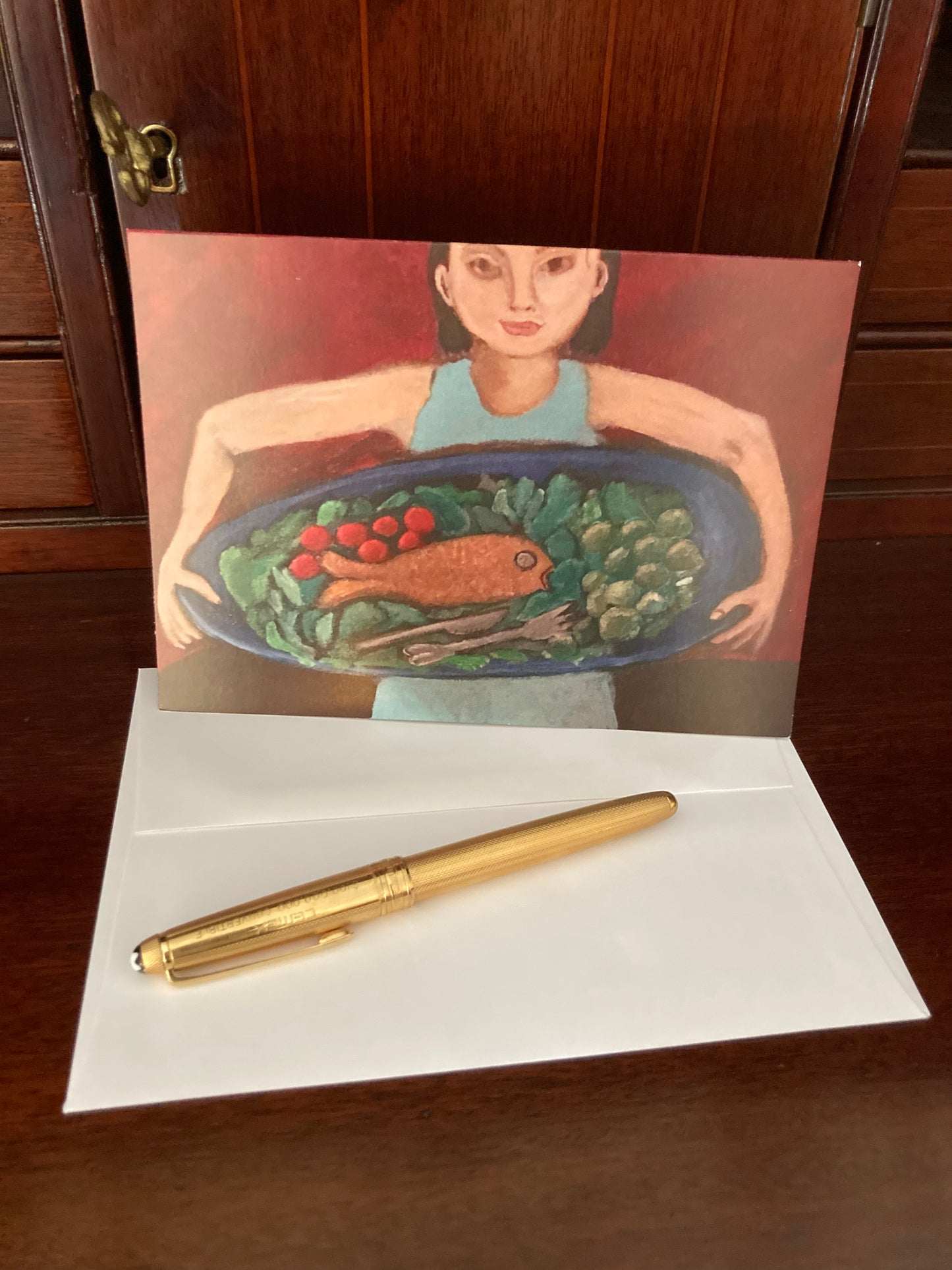 Mock up of the greeting card front along with its envelope and a gold pen displayed on a wooden desk.
