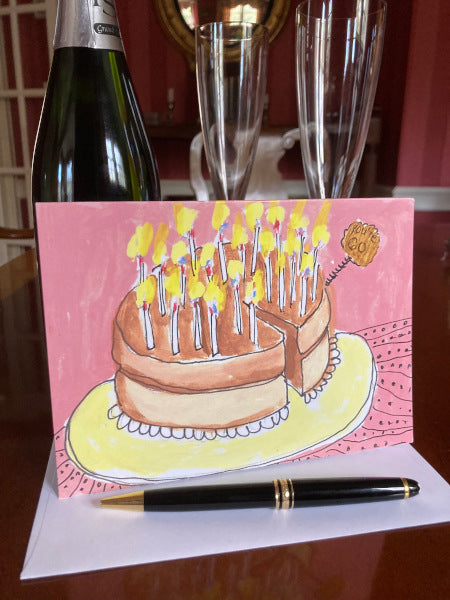 The front of the Card You're 60! displayed on a table top with a white envelope and black pen in the foreground and a champagne bottle and two champagne flutes visible in the background.