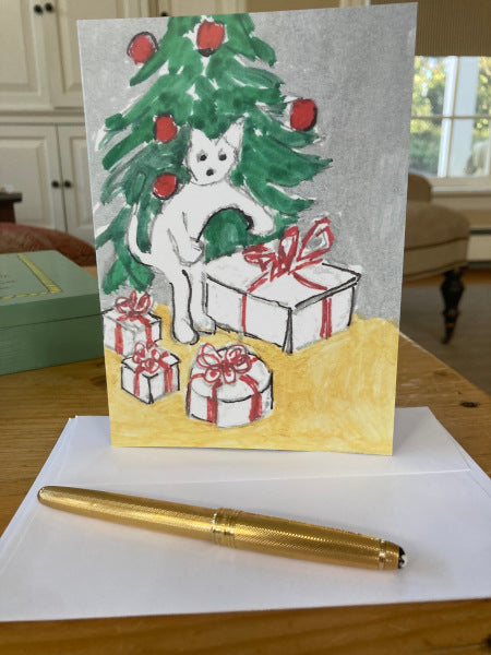 Photograph of the back of the card Little doings For Christmas standing upright on the desk with a partial view of the white envelope and a gold pen.