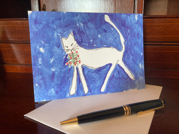 Photograph of the front of the greeting card Caspar Brings a Gift displayed on a brown desk atop a white envelope with a black pen lying nearby.