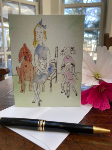 Front of the greeting card Mother's Day standing on brown table top with white envelope, black pen and a pink and a fuschia cosmos bloom.