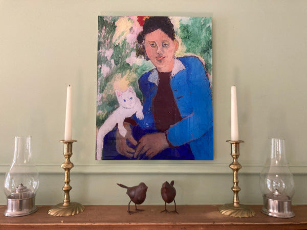 Mockup of the acrylic print titled Erica Blackwell With Caspar. This photograph shows the artwork hanging on a green wall flanked by brass candlesticks with white candles, two small glass and pewter hurricane lamps and two brown metal folk art birds to show the acrylic print in a home setting.