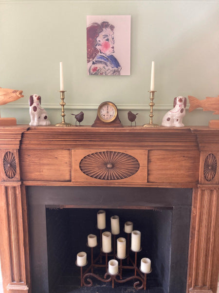 interior decor photo of the acrylic print portrait Jeanette hanging above a fireplace. This mockup shows the 11 x 14 artwork in realistic setting hanging on the light green wall in proportion to the the objects around it.