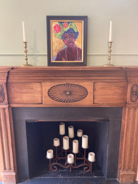 Mock up of Lady With Hat over the fireplace mantle in a black frame surrounded by two brass candlesticks.