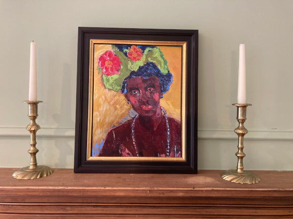 A mockup of the colorful portrait print is set on a wood mantle near a brass candlestick holding a white candle.