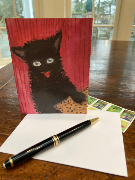 Front of the Happy Cat greeting card displayed on a brown tabletop with a white envelope, black pen and sheet of postage stamps.