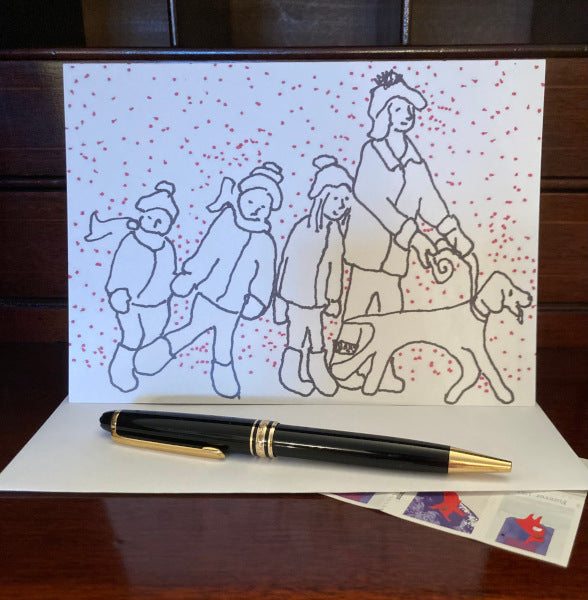 The front of the greeting card Hunter Leads The Way For A Fun Day is displayed on a brown desk with a white envelope, a black pen and a sheet of winter postage stamps peeking out from under the envelope.