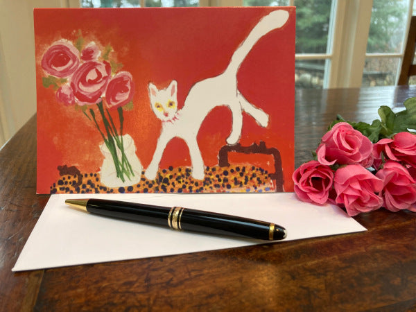 Mockup of the card on a wooden dining table with miniature pink roses, the envelope and a black fountain pen.
