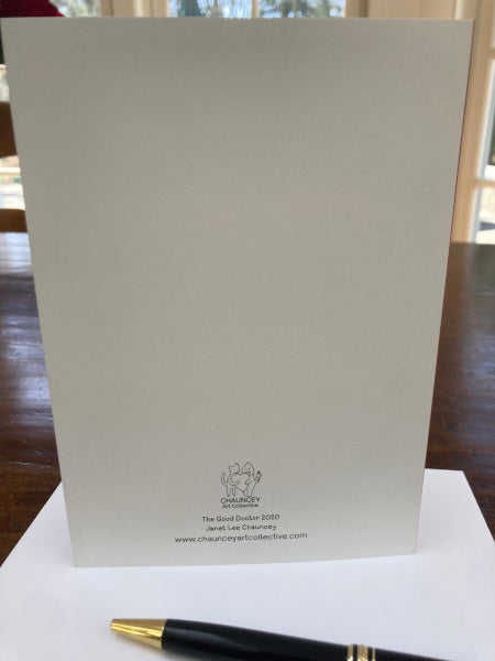 Mockup of the back of the greeting card, the Good Doctor standing upright on brown tale with envelope and black pen in foreground.