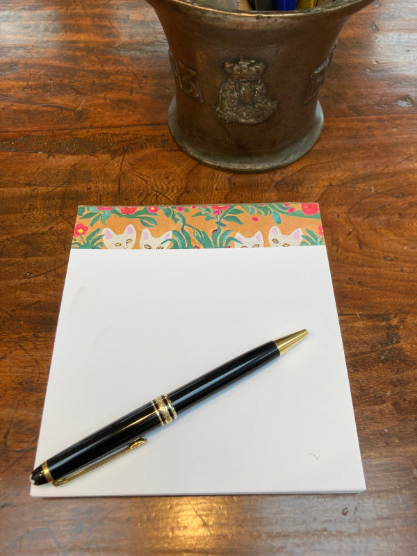 Mockup of Curious Cats on a wooden table with a black pen and a brass vase.