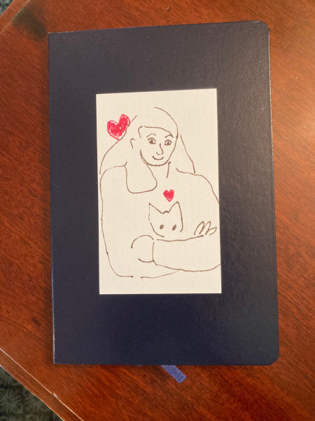 Armful of love journal stands out printed on a navy journal set against a wooden table. The sweet drawing shows pure love.
