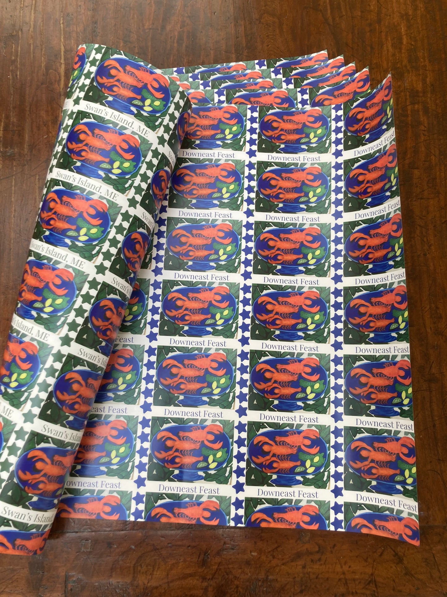 Mockup of gift box about to be wrapped in Swan's Island Wrapping paper, the paper curled to show the two patterns on the front and back sides. Give your gift downeast flair.