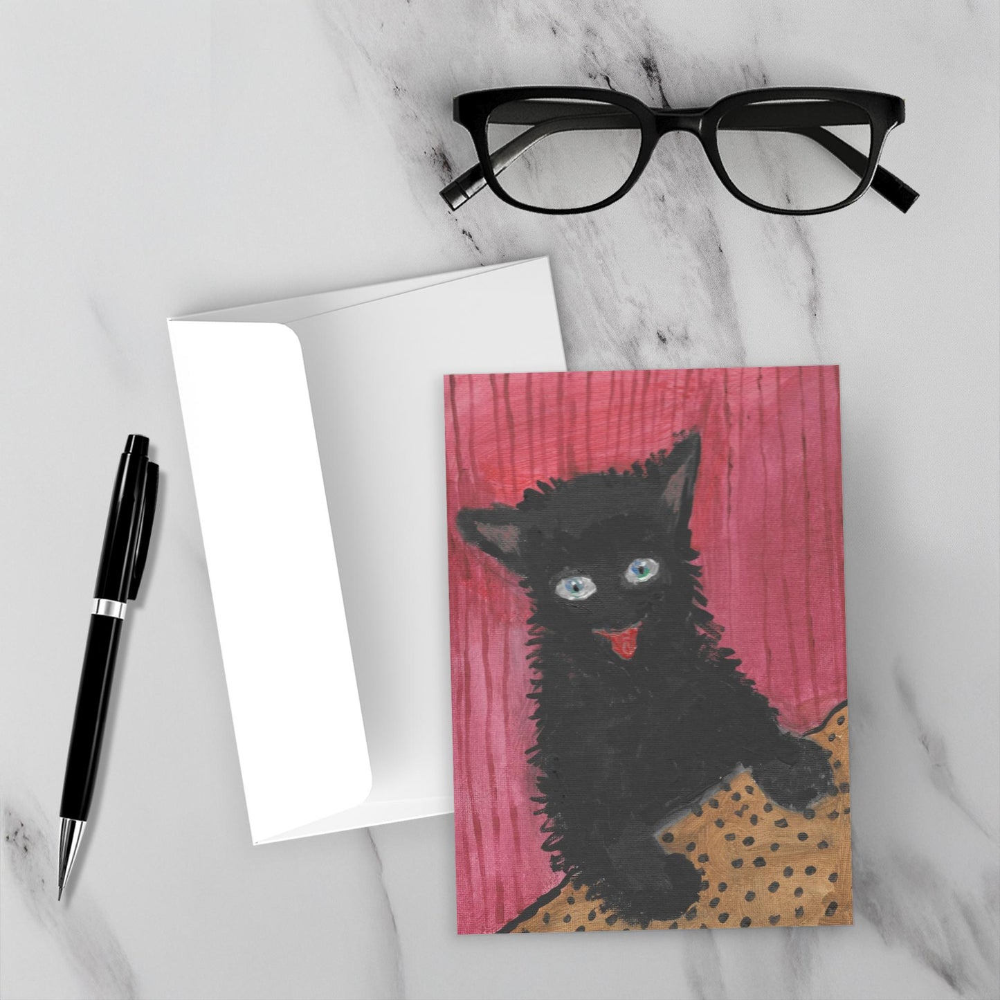 Mockup display showcasing the front of the greeting card Happy Cat lying on a gray marble surface along side a white envelope, a pair of black reading glasses and a black pen.
