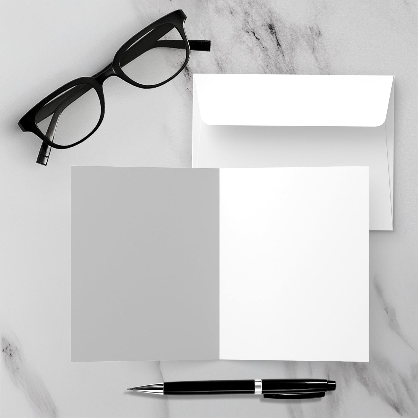 Mock up showing the blank inside of the greeting card Home Sweet Home along with the envelope. The background is a white marble surface with a black pen and reading glasses.