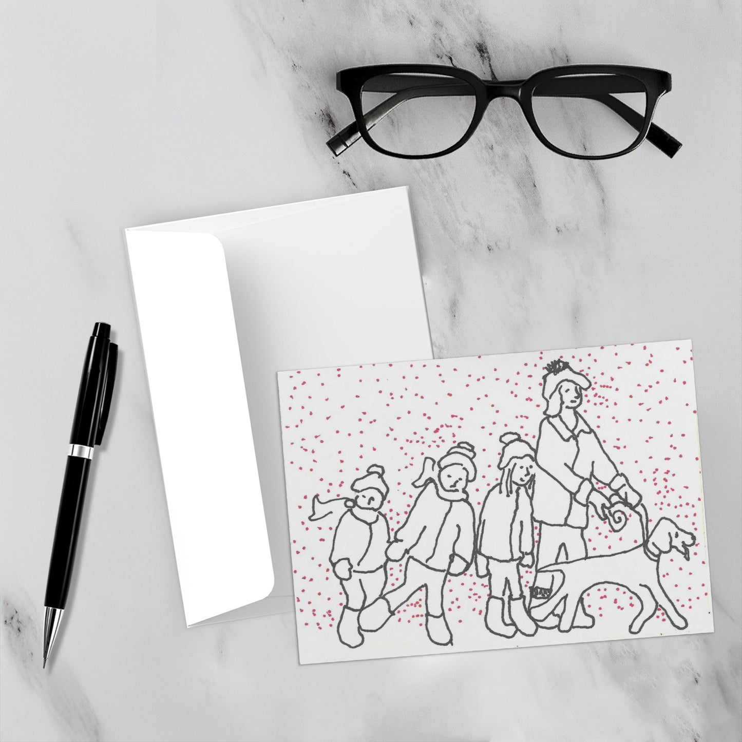 Mockup display showcasing the front of the greeting card Hunter Leads The Way For A Fun Day lying on a gray marble surface along side a white envelope, a pair of black reading glasses and a black pen.