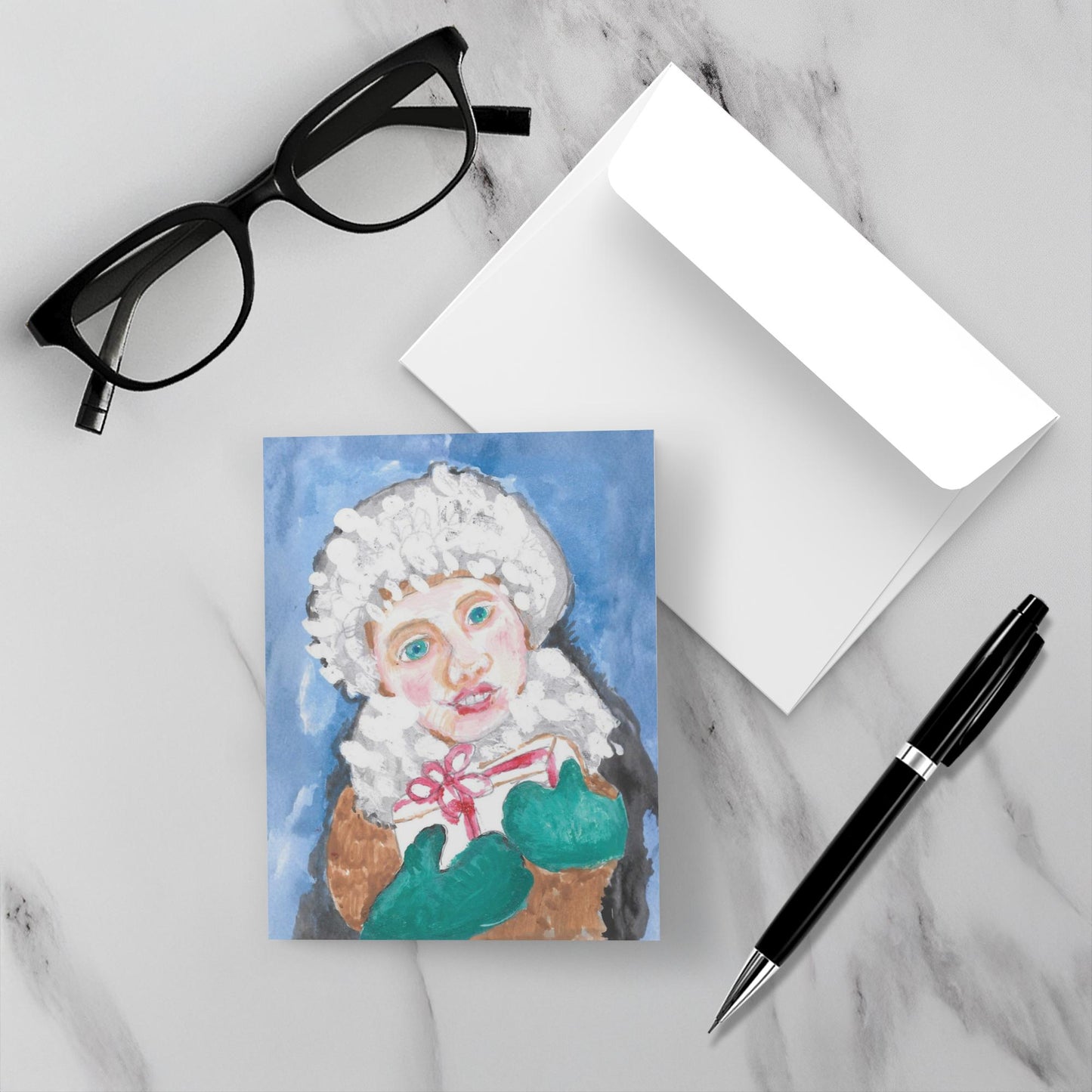 Greeting card with a painting of a joyous looking girl in a white hat and green gloves holding a present. The card is placed on a marble surface with glasses and a pen