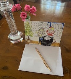 Mock up of Happy Birthday And All That Jazz card on a dining table with a crystal candlestick, a vase with miniature roses, the envelope and a gold pen.