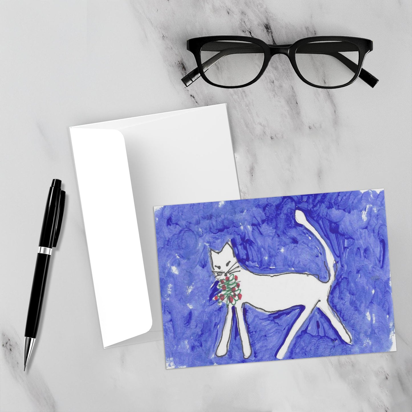 Mockup display showcasing the front of the greeting card Caspar Brings A Gift lying on a gray marble surface along side a white envelope, a pair of black reading glasses and a black pen.
