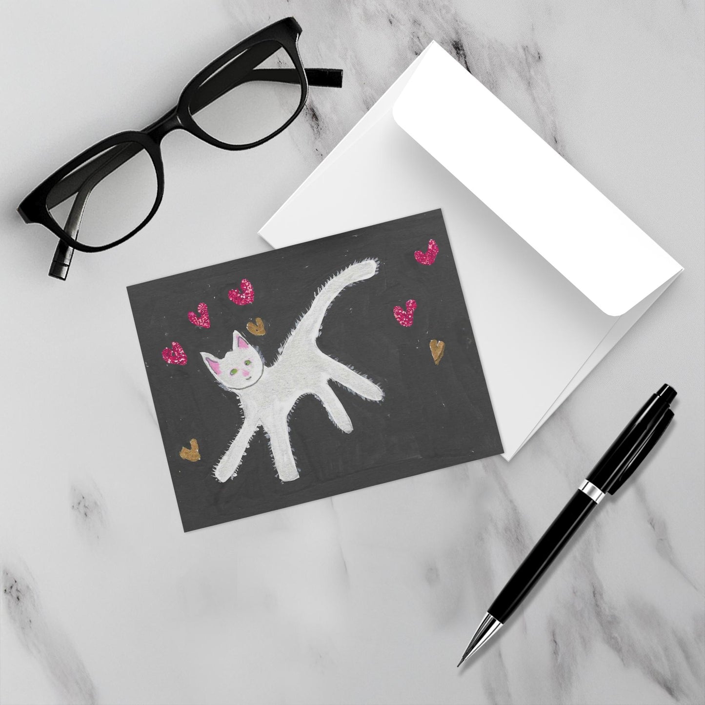 Mockup display showcasing the front of the greeting card Caspar With Floating Hearts lying on a gray marble surface along side a white envelope, a pair of black reading glasses and a black pen.