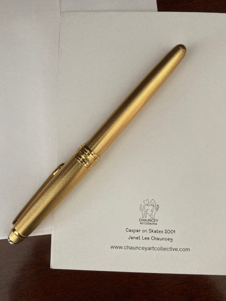 Photograph of the back of the greeting card lying flat on a brown desk top with partial view of white envelope and a gold pen.