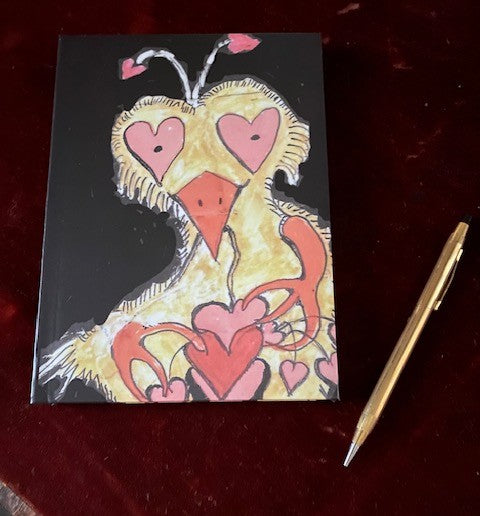 Photo of front of Crazy Heart Bird journal seen lying on the red velvet desk top beside a gold pen.