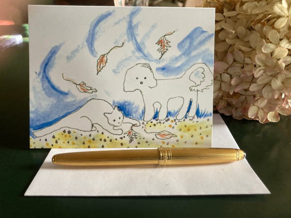 Mockup of the front of the greeting card Falling Leaves and the envelope with a gold pen and a hydrangea flower.
