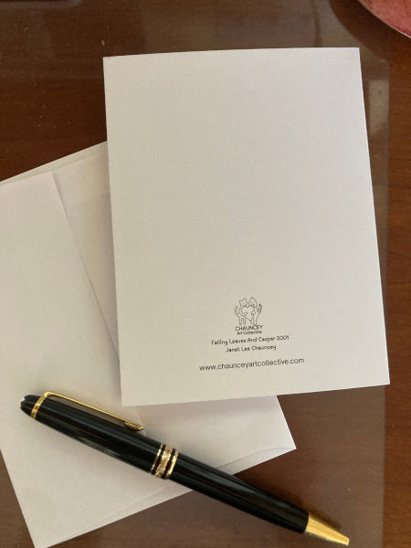 Photograph of the back of the card Falling Leaves And Caspar which shows the card lying on its white envelope n a brown desk top with a black pen across the bottom.