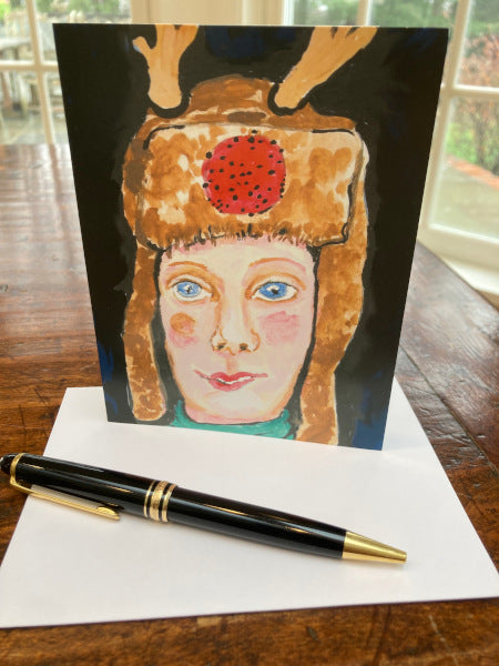 Photograph display of the front of the card of The Girl From Maine on a brown desktop with a white envelope and a black fountain pen.