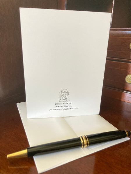 Back of the card displayed on a brown desk top so that you can see the logo and title with white envelope and a black pen in the foreground.