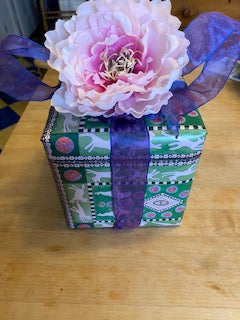 Mock up of Presentation Cats gift wrap with a purple bow and a large pink flower.