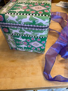 Mockup of gift wrapped in Presentation Cats wrapping paper. Showing the white cats running against the green background.