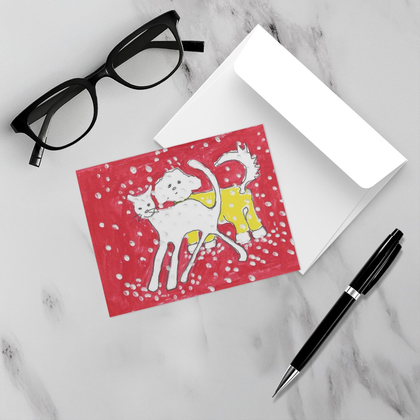 Mockup of the winter greeting card Jaunt In The Snow showing front of the card and its white envelope atop a grey marble surface with black eyeglasses on the top left and a black pen on the lower right.