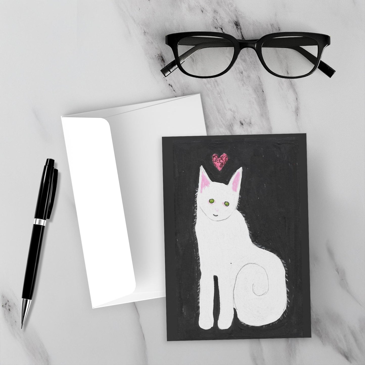 Mockup of the greeting card Love And Kisses Caspar really stand out against the white marble background. Envelope, pen and reading glasses are also shown.