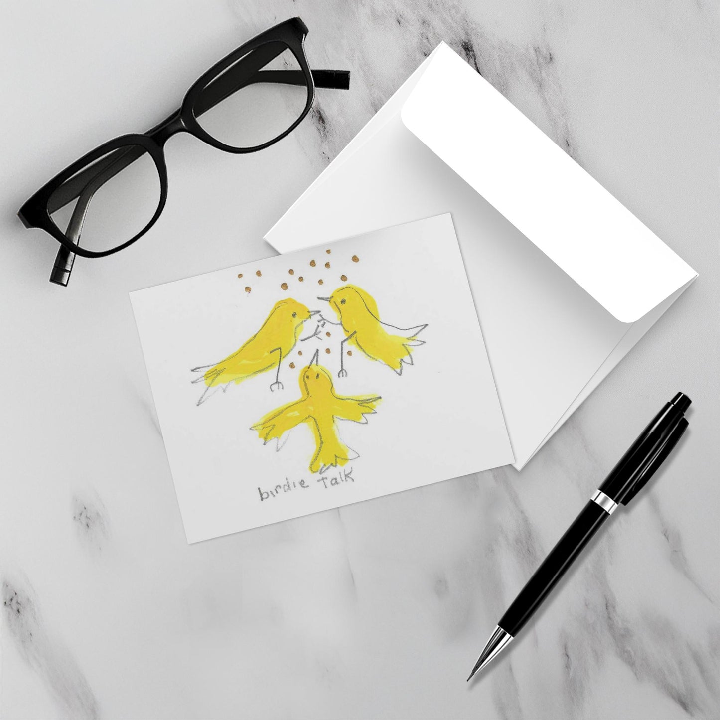 Mockup display showcasing the front of the greeting card Caspar Brings A Gift lying on a gray marble surface along side a white envelope, a pair of black reading glasses and a black pen.