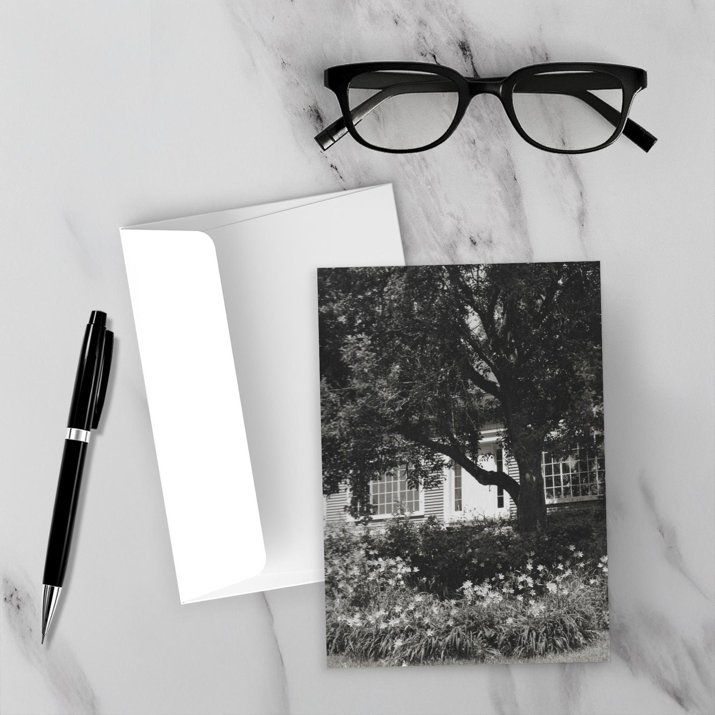 The front and back of the greeting card Home Sweet Home and the envelope surrounded by a black fountain pen and black reading glasses.
