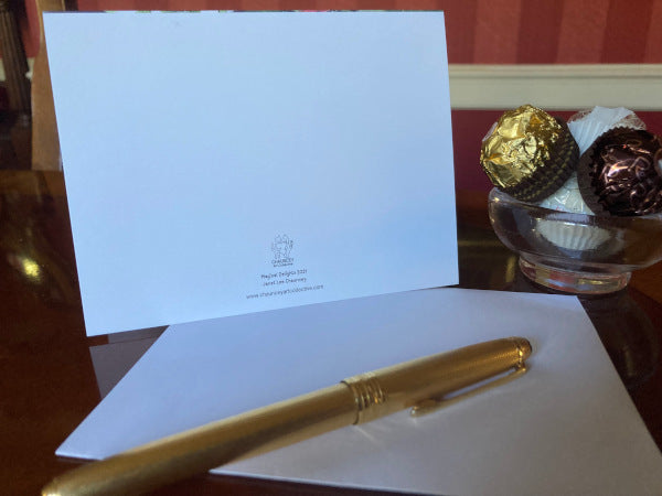 The back of the card is standing upright on a table with its envelope and a gold pen/