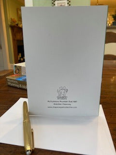 The back of the Card Mt. Rushmore Mountain Goat displayed on a brown desk with a white envelope and gold pen in the foreground and travel books just visible in the background.