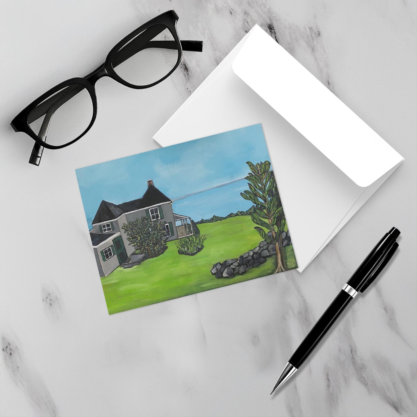 Mockup of greeting card Nutshell Cottage with envelope, reading glasses and pen on a white marble background.