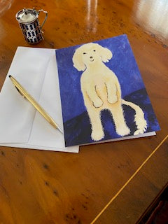 Back of greeting card Ollie Stands Up displayed on a brown tabletop with silver lidded cup, white envelope and gold pen.