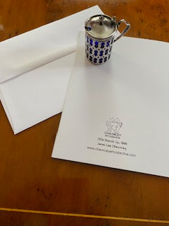 Back of greeting card on display showing the printed logo and title Ollie Stands Up along with a white envelope and a silver and blue lidded cup.