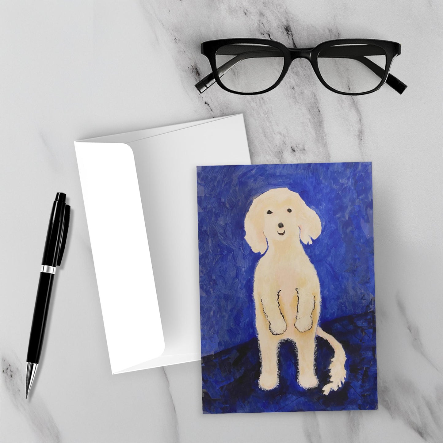Mockup display showcasing the front of the greeting card Ollie Stands Up lying on a gray marble surface along side a white envelope, a pair of black reading glasses and a black pen.