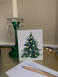Mockup of Outdoor Lights Christmas card with its envelope next to a green glass candlestick holding a white candle.