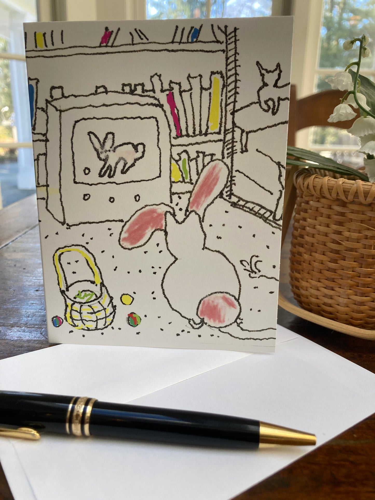 A mock up of the Easter Card standing up on its envelope next to a basket of white flowers.