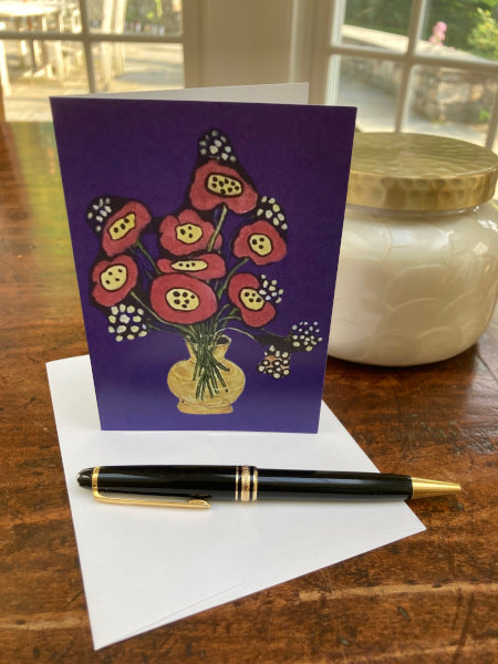 Mock up of the cheerful notecard Poppies In Yellow Vase is shown on a wooden table with the envelope and a black pen.